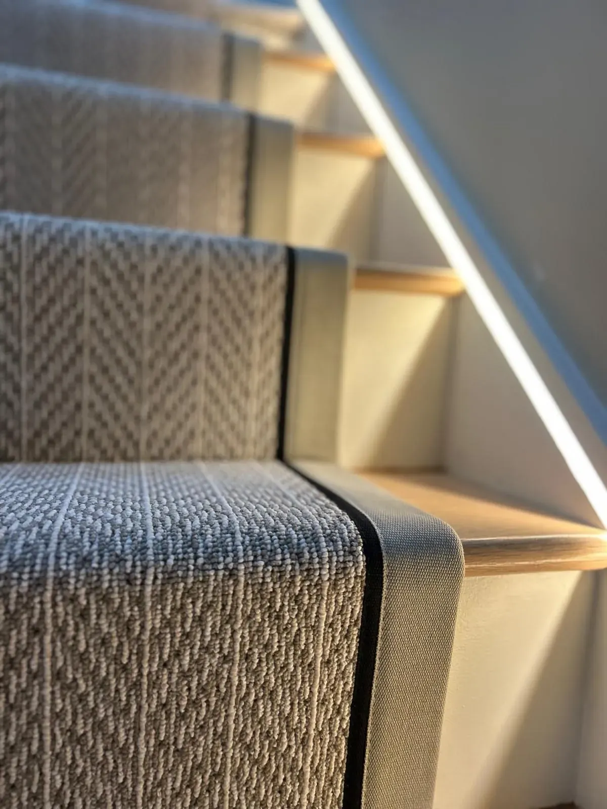 Close-up of a herringbone stair runner with bound edges on a lit staircase
